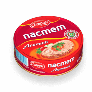 The image shows a red and orange tin can labeled with Cyrillic text. It features a logo that says Compass and the word пастет, indicating it is pâté. The can displays an image of the pâté spread on a slice of bread, garnished with parsley, a slice of tomato, and a cucumber. There is a barcode on the side, and the can is marked as a Bulgarian product with a weight of 180 grams.