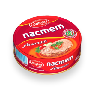 The image shows a round tin can of Compass brand pâté. The lid is predominantly red and displays the word пастет in large white letters. Below it, Апетит is written in a script font. There is a depiction of a slice of bread spread with pâté, garnished with tomato and parsley. The phrase Български продукт indicates it's a Bulgarian product. A barcode and weight (180g) are also visible on the side of the can.