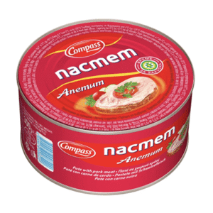 The image shows a can of Compass nacmem Anemum. The packaging is red with white text. There's an image of a slice of pate garnished with what appears to be herbs or greens. The can includes labels in multiple languages and indicates that it is a pate made with pork meat. There are also various symbols and certifications on the label.