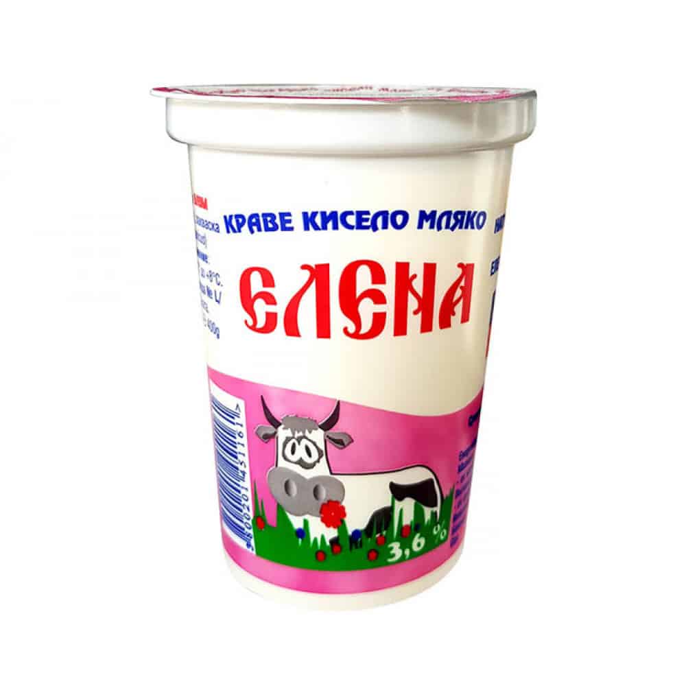 The image shows a yogurt container with a predominantly white body and a pink label. The text on the label is in Bulgarian, featuring the brand name prominently in red. There is an illustration of a cartoon cow on the label, standing on green grass with red flowers. The container is sealed with a plastic lid, and the yogurt's fat content, 3.6%, is noted on the label.