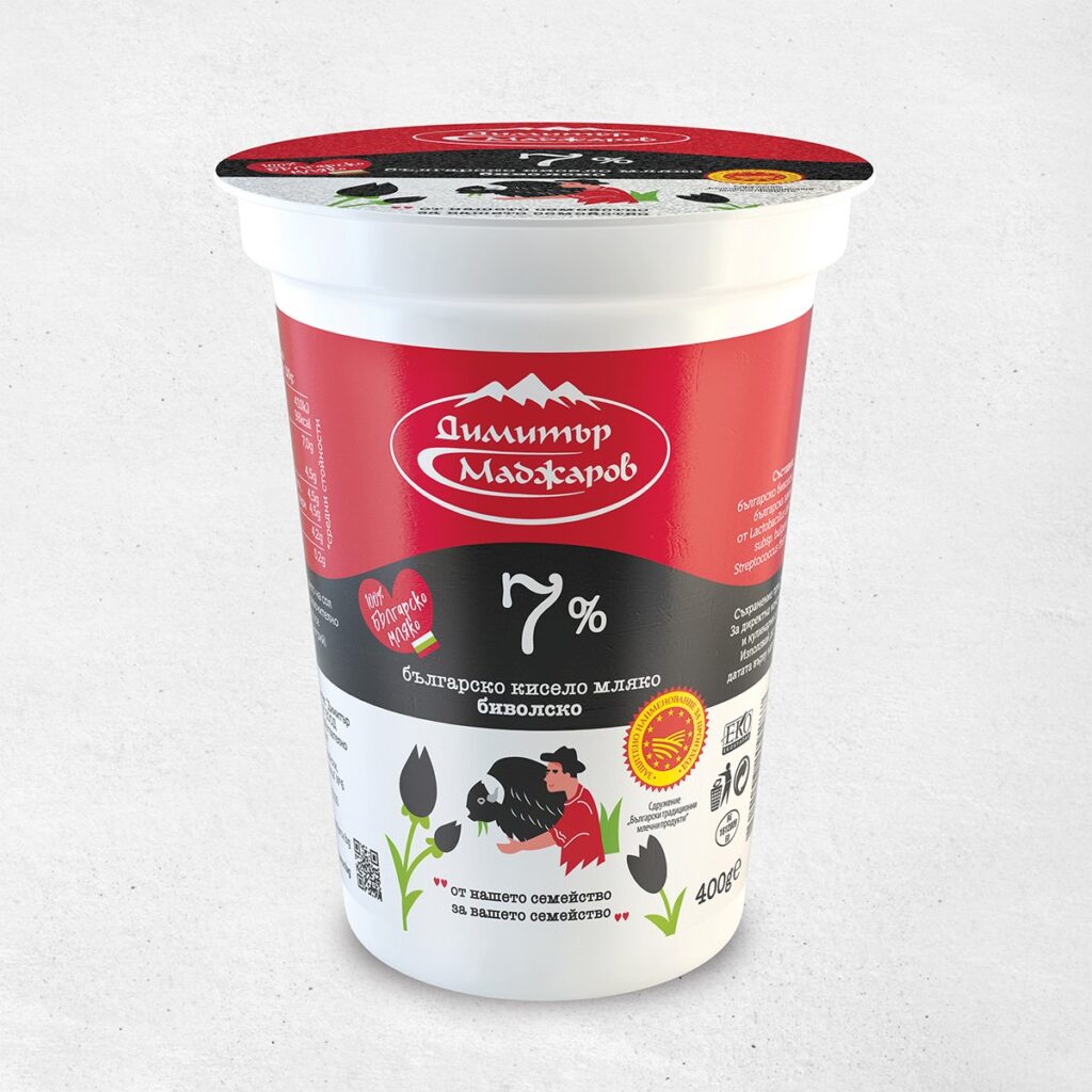 The image shows a container of Bulgarian yogurt with a red and black label. The brand name is in white text with a mountain logo above it. The label indicates 7% fat content in large white numbers. Below, there's an illustration of a person milking a buffalo. The container is 400g and features other design elements like tulips and certification logos. The text on the container is primarily in Bulgarian.