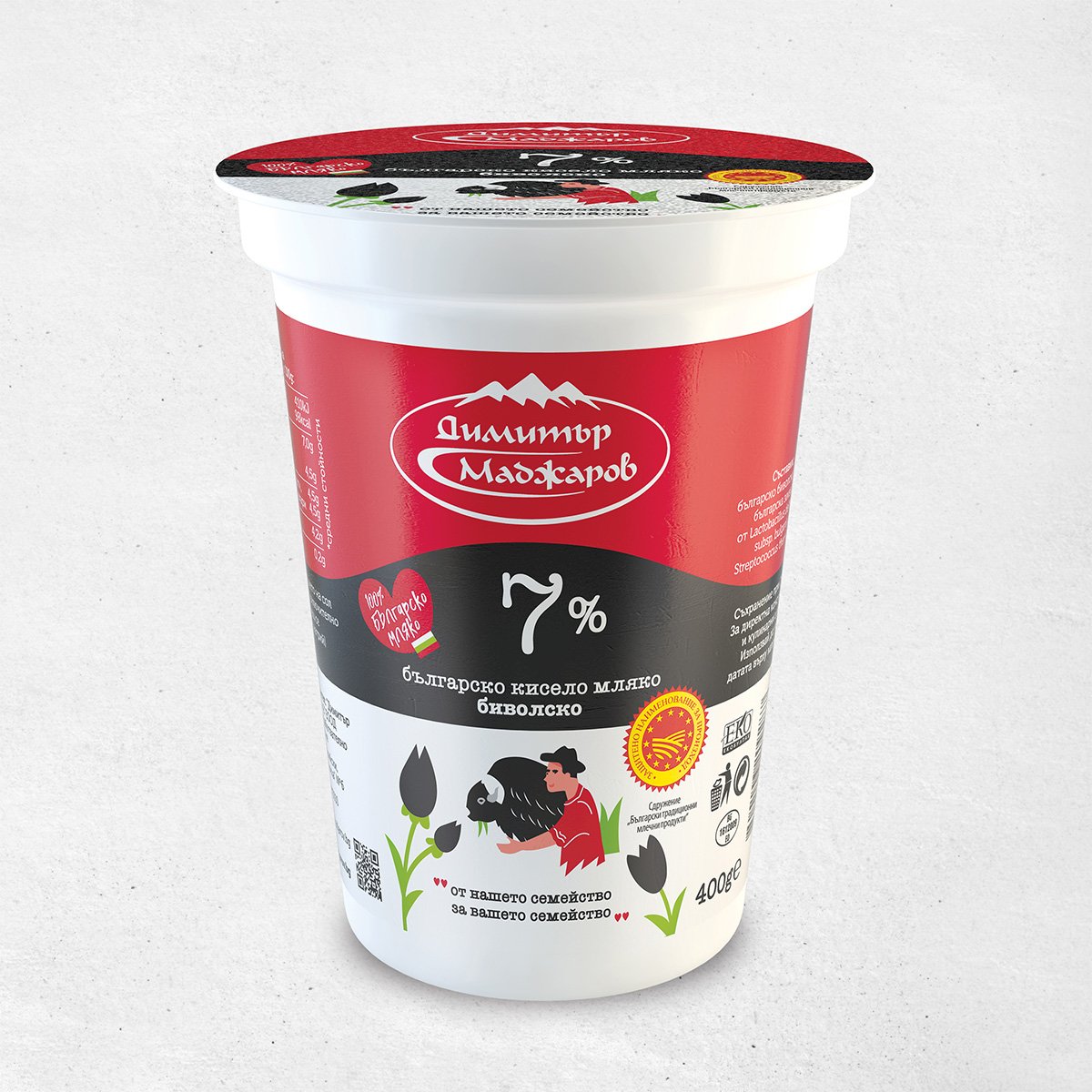 The image shows a container of Bulgarian yogurt with a red and black label. The brand name is in white text with a mountain logo above it. The label indicates 7% fat content in large white numbers. Below, there's an illustration of a person milking a buffalo. The container is 400g and features other design elements like tulips and certification logos. The text on the container is primarily in Bulgarian.