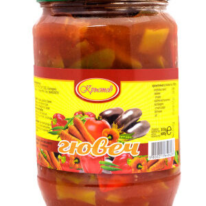 The image shows a glass jar with a green lid, containing a vegetable stew in a red sauce. The label is yellow with red borders and features images of eggplant, tomatoes, and bell peppers, along with the brand name and product information in a Slavic language. The word лювец is prominently displayed on the label.