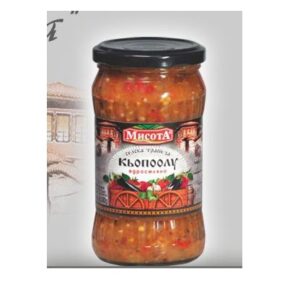 The image shows a jar of a food product with a black lid. The contents inside appear to be a vegetable-based dish, possibly a spread or salad. The label features traditional design elements and includes text in a Cyrillic script. The name Мисота is prominently displayed, along with an illustration of a dish with peppers or similar vegetables. The label conveys a traditional or rustic theme.