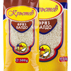 The image shows two packages of rice. Both packages have a similar design with yellow and brown colors. The brand name is displayed prominently at the top inside an oval shape. Below the brand name, there is a clear window showing the rice grains. The text on the package reads ориз балдо, indicating the type of rice. The smaller package is labeled 500g, and the larger one is labeled 1kg. Both packages feature a small, colorful illustration of a chicken in a circular design near the bottom.