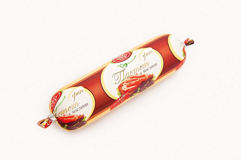 The image shows a packaged sausage-shaped product, possibly a type of pate. The packaging is colored in shades of red and orange with a white oval label. The label includes images of olives and a pâté spread on bread. Cyrillic text is present, suggesting a non-English language, possibly advertising olives as a key ingredient. The ends of the packaging are twisted and sealed.
