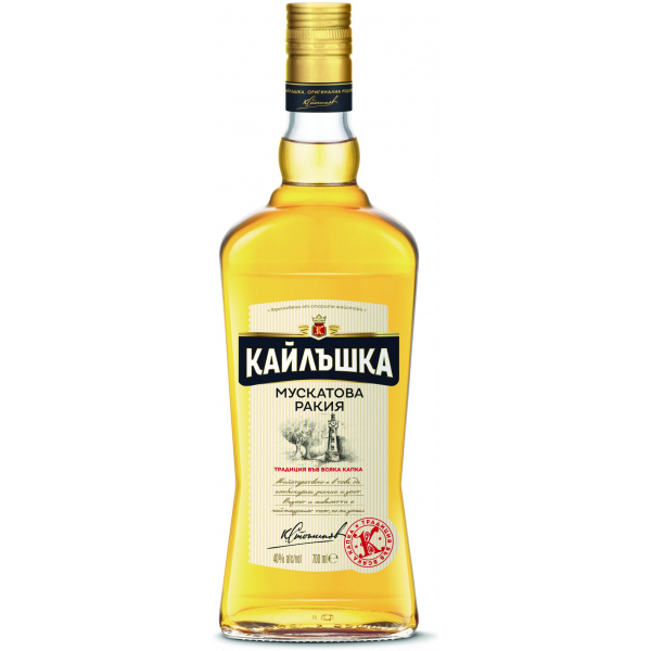 This is an image of a bottle of Кайлъшка Мускатова Ракiя, a type of muscat rakia. The bottle is transparent and has a golden amber liquid inside, with a black and gold cap. The label is cream-colored with black and gold detailing, featuring Cyrillic text. There's an emblem at the top and a signature at the bottom, accompanied by a red seal. The bottle size is indicated as 500ml with 40% alcohol by volume.
