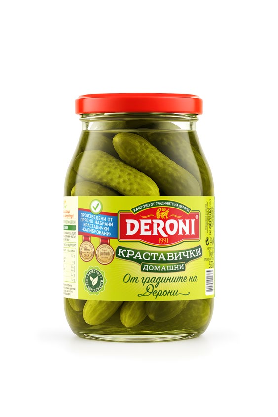 The image shows a glass jar of pickled cucumbers. The label on the jar is primarily green and yellow with red accents. The brand name Deroni is prominently displayed in white text on a red background. The top of the jar is sealed with a red lid. Various text in Cyrillic is present, suggesting the product is from Bulgaria. The label also includes some icons and badges, likely indicating quality or certifications. The cucumbers are visible through the clear glass of the jar.