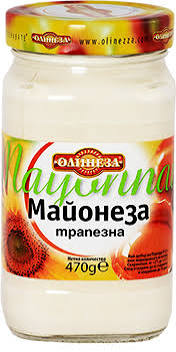 The picture shows a glass jar of mayonnaise. The label has a colorful design with the brand name Olinezza prominently displayed. The text on the label includes the word Майонеза, indicating it's mayonnaise, along with трапезна, which translates to table mayonnaise in Bulgarian. The contents of the jar are 470 grams. There is a sunflower image on the label, and the lid is yellow with the brand name repeated around the edge.