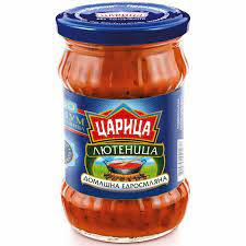 The picture shows a jar of a red sauce called Лютеница. The label has a blue background with red and green accents. There is a logo featuring a stylized design and the words Царица and Домашна едросмляна below the name. The jar has a blue lid with white text printed on top.