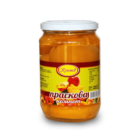 The image shows a glass jar with a white lid containing preserved peaches. The label on the jar is predominantly yellow with red accents. It features images of peaches and text in Cyrillic script. The contents appear to be peach compote, visible through the clear glass.