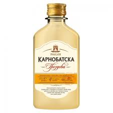 The image shows a bottle of Карнобатска Гроздова rakia. The bottle has a gold screw cap and a clear amber liquid inside. The label is white with gold and black text, featuring a crown logo at the top. It includes a decorative emblem and additional text in Bulgarian below. The bottom section of the label is orange with more details, likely about the product.