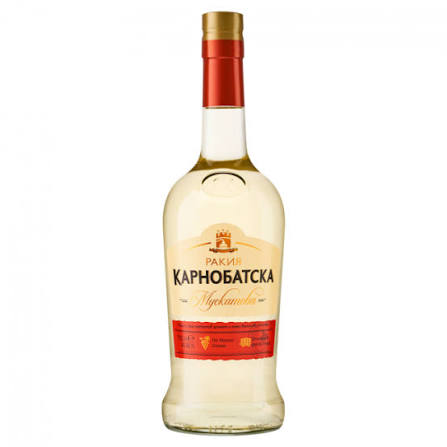 The image shows a bottle of Karnobatska Rakia. The bottle is transparent with a light-colored liquid inside. It has a red cap and a label featuring a combination of beige and red colors. The label includes Cyrillic text and decorative elements. The design also incorporates logos and additional text beneath the main label.