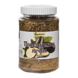 The image shows a jar with a white lid containing a chunky, brownish mixture. The label has green and white colors, featuring images of eggplants. There is text in a non-Latin script, possibly describing roasted eggplant or similar contents. The contents appear to be preserved or pickled.