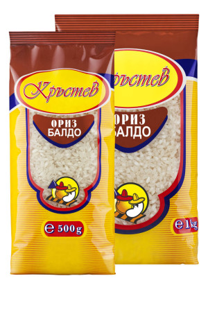 The image shows two packages of rice with identical designs, featuring a brownish top and a yellow bottom. The brand name is written in a decorative script within an oval, highlighted by red and blue colors. Below the brand, there is a description of the rice in Cyrillic script on a dark background. Each package has an illustration of a cartoonish chicken wearing a chef's hat. The weights are marked as 500g on the smaller package and 1kg on the larger one. The packages are transparent in the middle, revealing the rice inside.